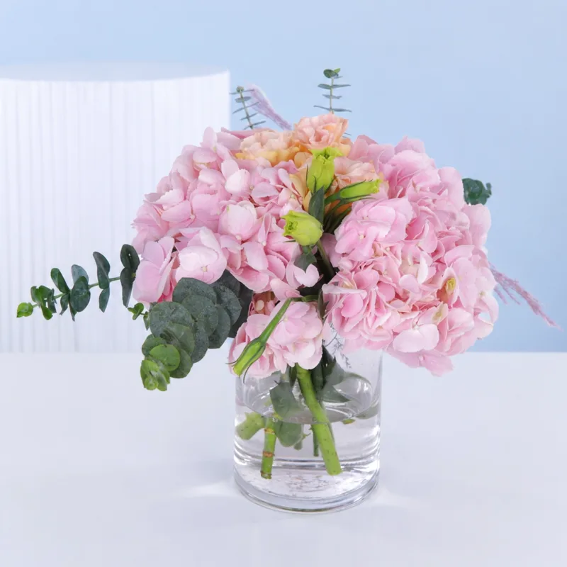pastel-pink-vase-arrangement Cylindrical glass vase centerpiece featuring soft pink hydrangeas and lisianthus arranged for elegant table decor and refined event styling.