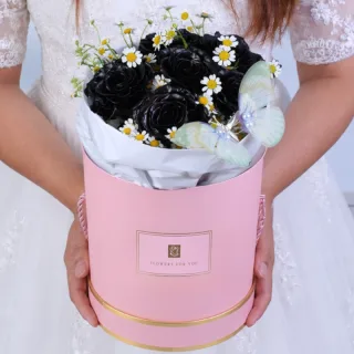 Luxurious box featuring seven black-painted roses, fresh white tanacetum flowers, and a butterfly nestled among the blooms, creating a dramatic and sophisticated floral presentation.