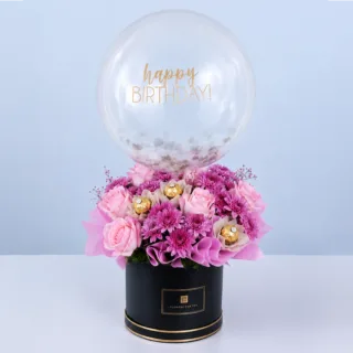 Pink-themed bouquet in a black round box featuring roses, chrysanthemums, Ferrero Rocher chocolates, and a balloon arranged as a luxurious celebration gift.