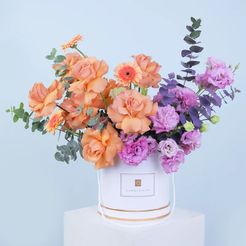 blooms-for-you-hat-box Blooms For You Hat Box featuring fresh peach roses, peach gerberas, purple lisianthus, and eucalyptus beautifully arranged in a premium hat box.
