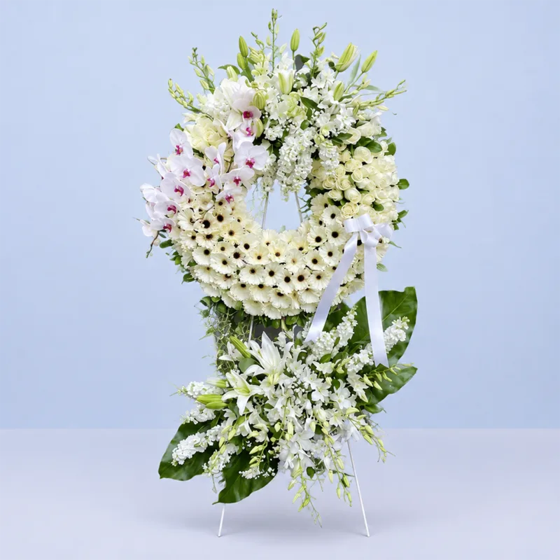 eternal-white-wreath-stand Eternal White Wreath Stand featuring white gerberas, white phalaenopsis orchids, white roses, white lilies, white matthiola, white hydrangeas, gypsophila, and fresh greenery arranged in an elegant white sympathy wreath stand.