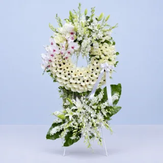 Eternal White Wreath Stand featuring white gerberas, white phalaenopsis orchids, white roses, white lilies, white matthiola, white hydrangeas, gypsophila, and fresh greenery arranged in an elegant white sympathy wreath stand.