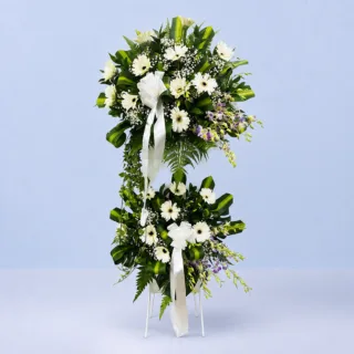 White & Purple Condolence Stand featuring white gerberas, purple orchids, gypsophila, massangeana, Singapore leaves, Hartera, and single ruscus arranged on a white steel sympathy flower stand.