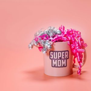 a light pink ceramic mug with the words "SUPER MOM" printed on the side in a bold, outlined font.